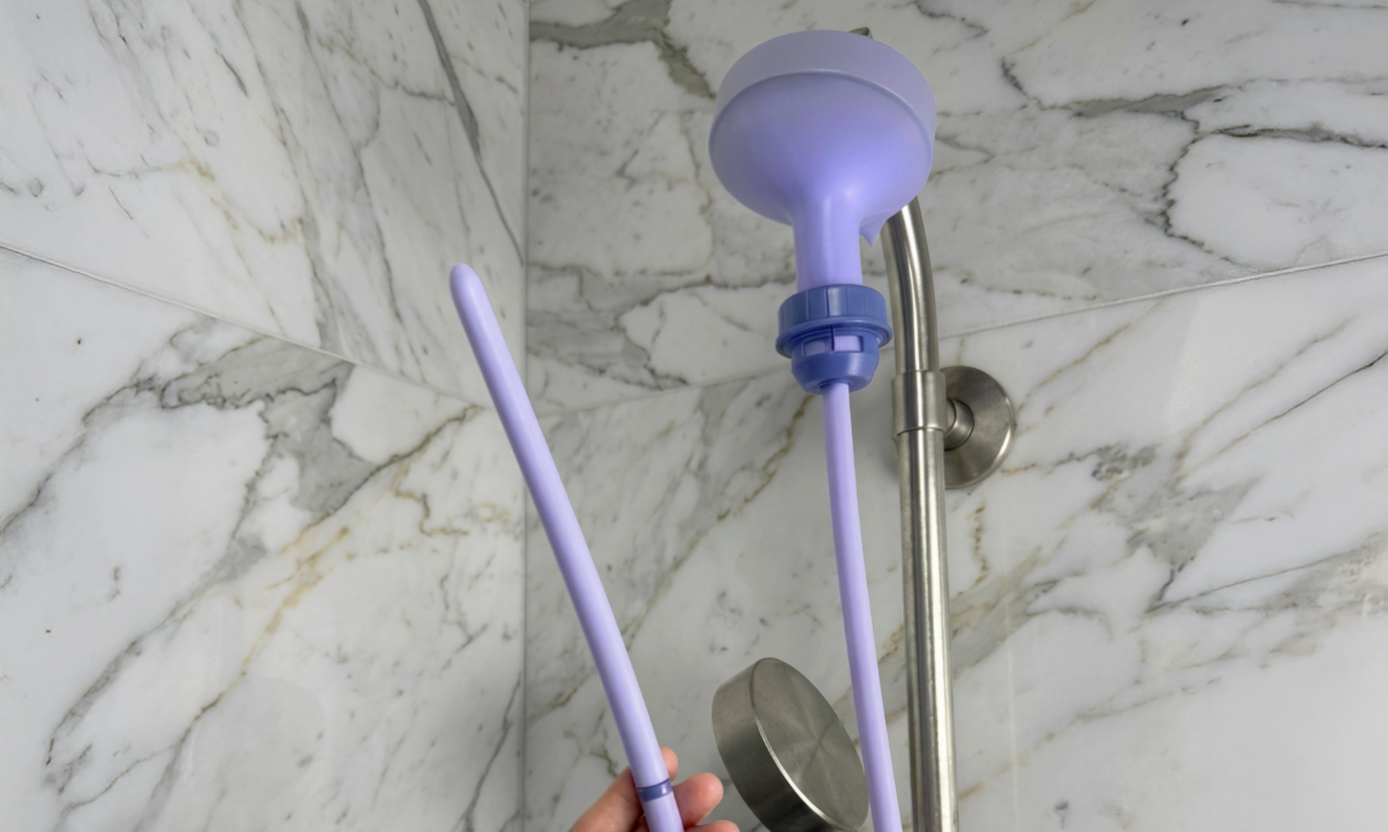 Purple Squwash Douche attached to shower head and hose held by a hand against a marble bathroom wall.